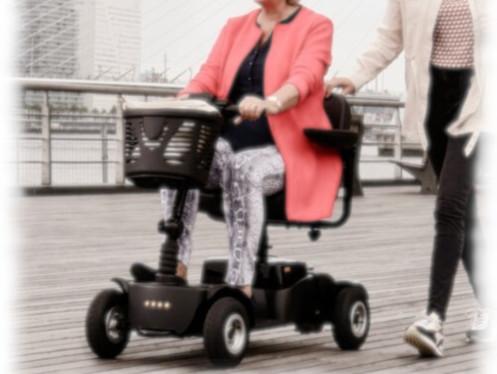 Vrouw in elektrische scooter met iemand die ernaast loopt