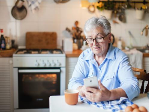 Vrouw zit aan tafel met gsm in de hand in de keuken