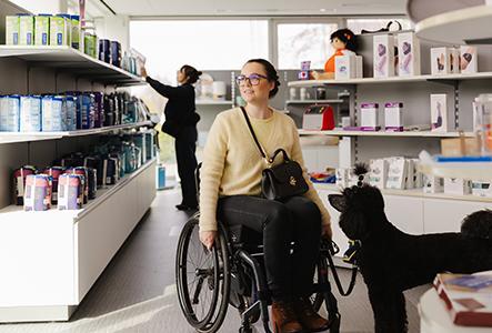 Klant in een rolstoel bezoekt een Helan Zorgwinkel en bekijkt het aanbod rond hulpmiddelen en verzorgingsproducten in de winkel