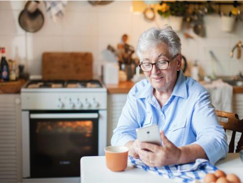 Vrouw bekijkt ontspannen haar smartphone in de keuken terwijl ze geniet van een warme koffie en voordeelacties ontdekt